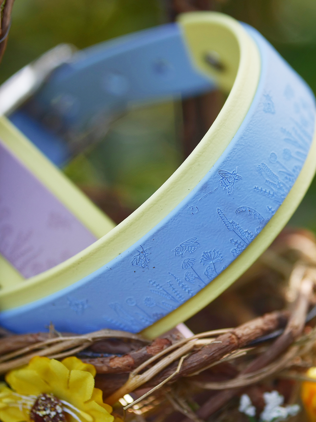 Pastel blue Bees and Blooms hound collar with yellow backing resting in a decorative basket surrounded by spring flowers